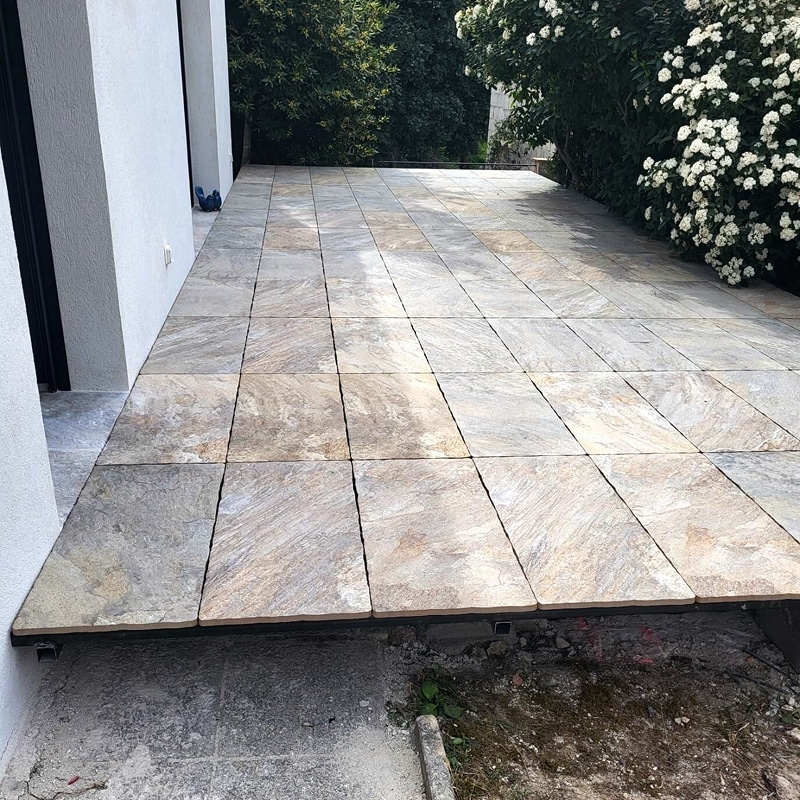 Dalles de carrelage extérieur aspect pierre pour terrasse Terrasse moderne avec carrelage de grandes dalles aspect pierre naturelle, près d'un mur blanc et jardin verdoyant.