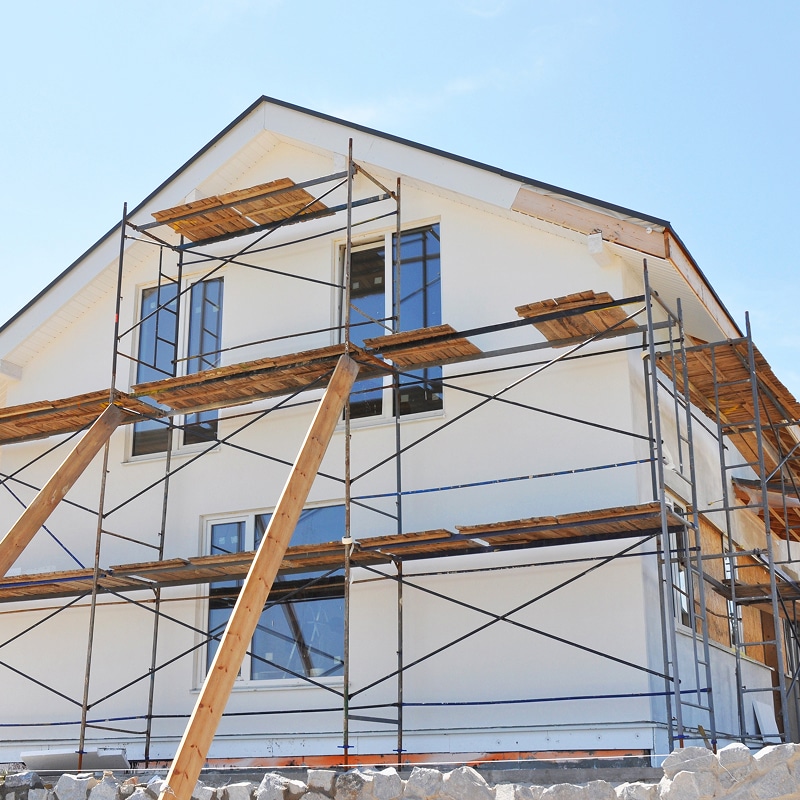 Échafaudage de Maison : Travaux de Construction/Rénovation Maison blanche neuve ou en rénovation avec échafaudage métallique et planches de bois. Travaux de façade sous ciel bleu dégagé.