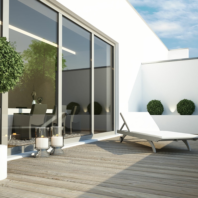Terrasse Design Moderne et Portes Vitrées Coulissantes. Terrasse extérieure design avec deck en bois, grandes portes vitrées, chaise longue blanche et arbustes décoratifs.