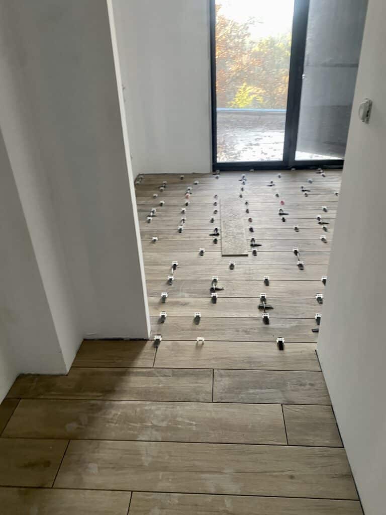 Pose carrelage imitation bois avec croisillons chantier Pose de carrelage imitation bois en cours, avec des croisillons pour l'espacement sur un sol clair, devant une grande baie vitrée.