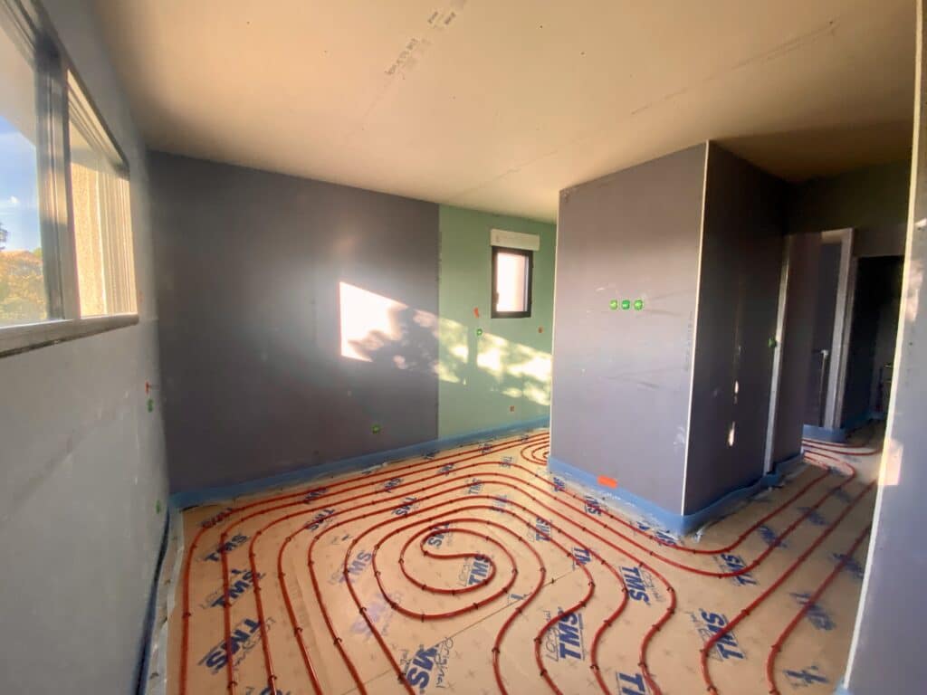 Installation Chauffage au Sol : Pose Tuyaux TMS Chantier intérieur : pose de chauffage au sol (tuyaux rouges TMS) sur plaques isolantes avant chape, murs peints gris et vert.
