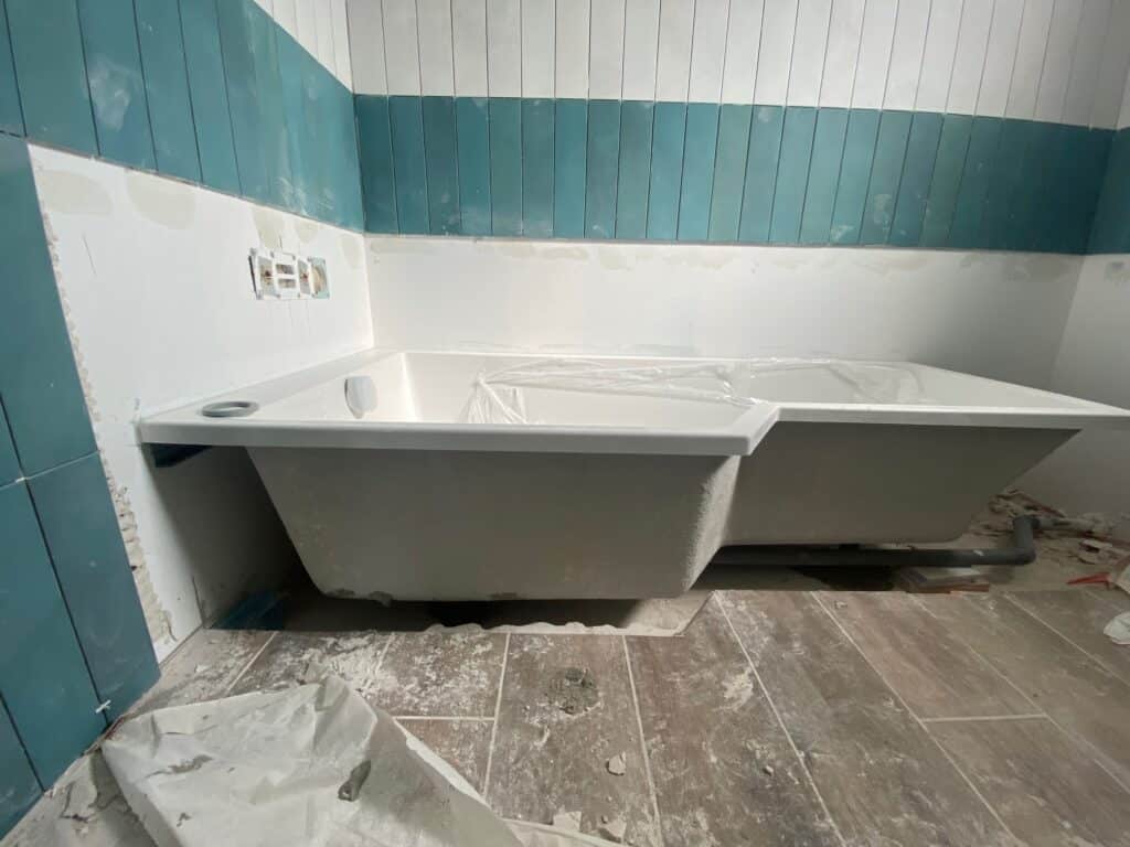 Baignoire blanche en coin en cours d'installation dans une salle de bain en rénovation avec carrelage mural bleu et blanc.
