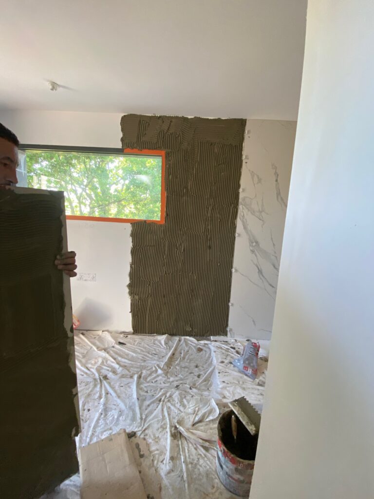 Pose de carrelage mural grand format effet marbre par un artisan carreleur dans un intérieur en rénovation.