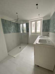 Salle de bain moderne en rénovation avec douche à l'italienne vitrée, double vasque blanche et carrelage mural bleu.