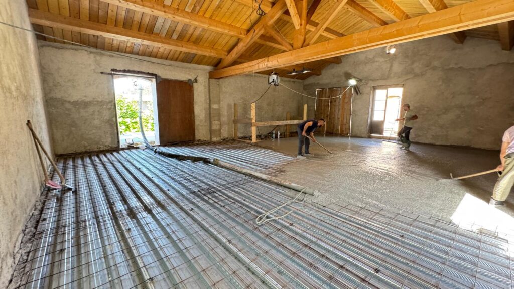 Ouvriers étalant du béton sur plancher métallique et treillis sous une charpente bois.