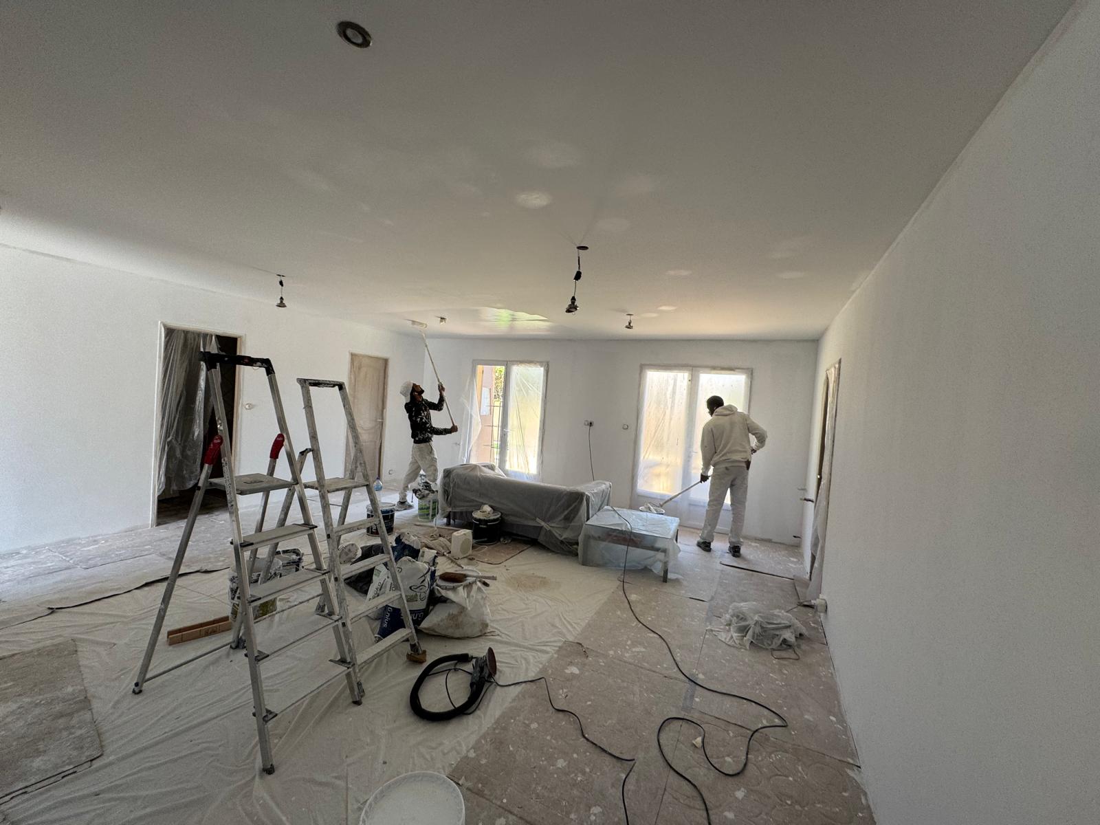 Peintres professionnels peignant un plafond et des murs blancs dans un salon en rénovation avec échelles.
