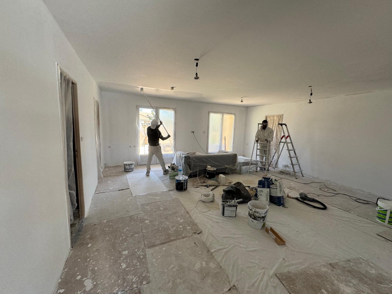 Peintres appliquant de la peinture blanche sur les murs et le plafond d'un salon en rénovation.